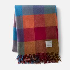 a multicolored plaid blanket with fringes on the ends and a tag hanging from it