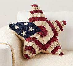 an american flag pillow sitting on top of a white couch with red, white and blue ruffles