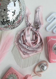 a pink phone, scarf and mirror on a white table with other items around it