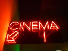 a neon sign that says cinema on the side of a building in front of a red light