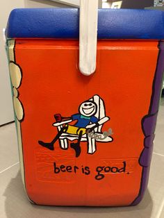 an orange and blue cooler with a cartoon character sitting on it's seat that says beer is good