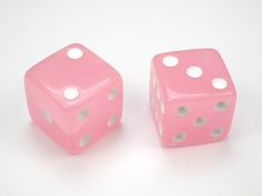 two pink dices sitting side by side on a white surface with holes in the middle