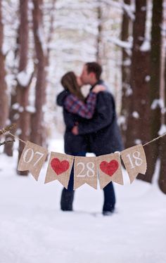 a man and woman kissing in the snow next to a banner with hearts on it