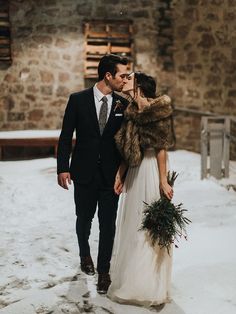 a bride and groom are standing in the snow with their fur stole around their shoulders