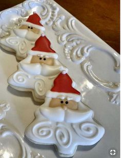 three santa clause cookies sitting on top of a white platter with swirly icing