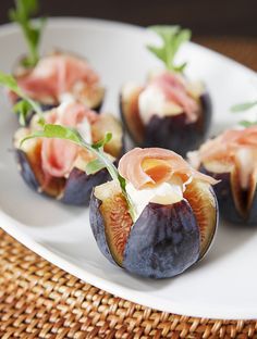 figs with prosciutto and cream cheese on a white plate next to a woven place mat