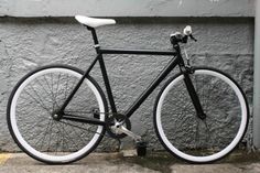 a black and white bicycle parked next to a gray wall with no people on it