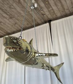 a large metal fish hanging from a ceiling in front of a white curtained wall