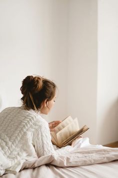 a woman sitting on a bed reading a book