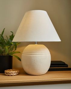 a white lamp sitting on top of a wooden table next to a potted plant