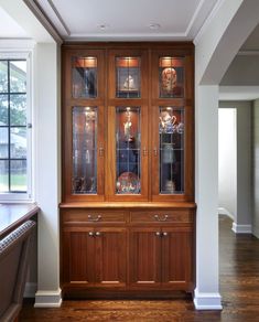 a wooden china cabinet with glass doors in the middle of a room next to a window