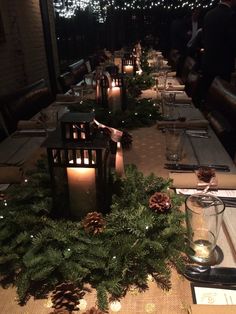 a long table is set with candles and pine cones for christmas dinner guests can also be seen in the background