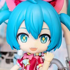 a close up of a doll with blue hair and big eyes wearing a pink dress