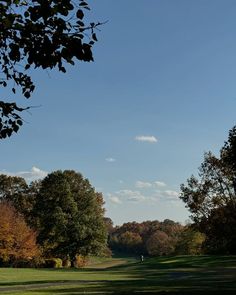 a person walking in the distance on a golf course with trees and blue sky behind them