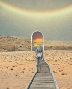 a woman walking down a wooden walkway in the desert with a rainbow painted on it