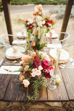 a wooden table topped with lots of flowers and greenery on top of white plates