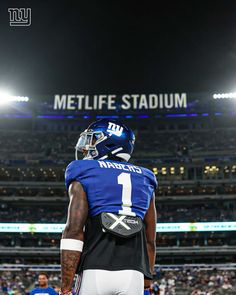 a football player standing on top of a field wearing a blue and white uniform with the words metlife stadium in the background