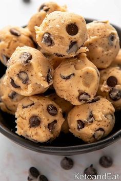 chocolate chip cookie dough bites in a black bowl on a white table with scattered chocolate chips