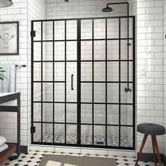 a black and white tiled bathroom with glass shower door, stools and towel rack