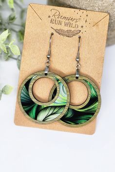 a pair of earrings with green leaves on the front and back, hanging from a card board