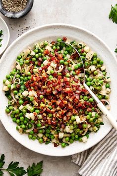 a white bowl filled with peas and bacon next to some parsley on the side