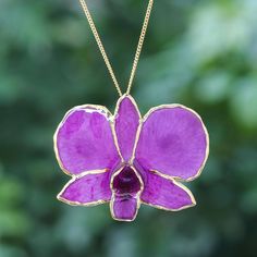 a large purple flower is hanging from a gold plated necklace that has a chain attached to it