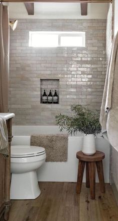 a white toilet sitting next to a bath tub in a bathroom on top of a hard wood floor