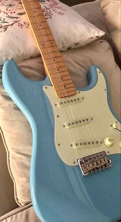 a blue electric guitar sitting on top of a couch next to pillows and pillow cases