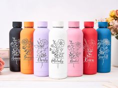 thermos bottles are lined up next to each other on a white table with flowers