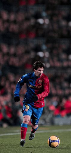 a soccer player is running with the ball in front of him and people watching from the stands