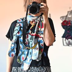 a woman holding a camera up to her face while wearing a scarf around her neck