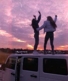 two women standing on top of a white vehicle in the sunset with their arms up