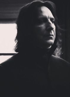 a man with long hair standing in front of a window looking off into the distance