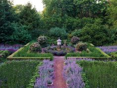 a garden with lots of plants and flowers on the sides of it, surrounded by trees