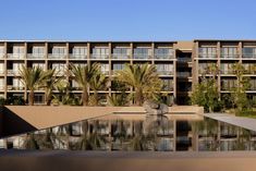 an apartment building with palm trees in front of it and a reflecting pool on the ground