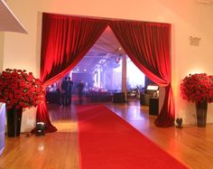 a red carpeted hall with two vases filled with flowers on each side and an open door leading to another room