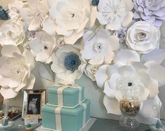 a table topped with lots of white flowers and cake next to a wall covered in paper flowers