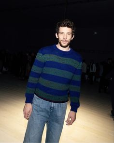 a man standing in front of a wooden floor wearing a blue and green striped sweater