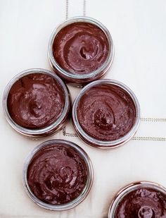 four jars filled with chocolate pudding sitting on top of a white cloth covered tablecloth