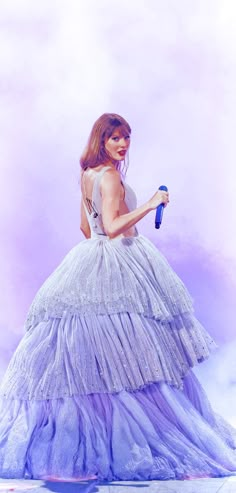 a woman in a white dress holding a blue umbrella and wearing a purple gown with ruffled layers