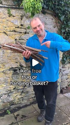 a man standing next to a stone wall holding a bunch of sticks in his hands