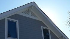 the top of a house with two windows and a bird flying in the sky above it