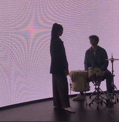 two people are standing in front of a large screen and playing drums on the floor