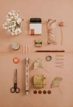 an assortment of crafting supplies laid out on a pink surface with flowers and scissors