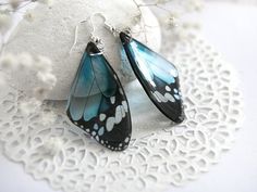 a pair of blue and black butterfly earrings sitting on top of a white doily