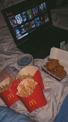 a laptop computer sitting on top of a bed next to two trays of food