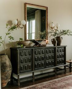 a living room with a large mirror and vases on top of the sideboard