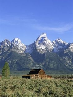 an old barn in the middle of a field with mountains in the background