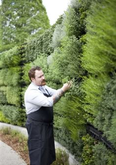 a man standing next to a lush green wall