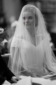 a woman sitting at a table wearing a wedding veil and holding a book in her hand